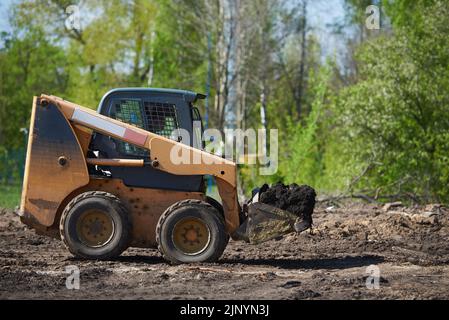 La minipelle sur pneus travaille dans le jardin, transporte le sol Banque D'Images