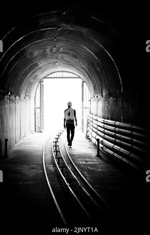 Silhouette d'un jeune homme qui sort d'un tunnel sombre pour entrer dans une lumière vive. Banque D'Images