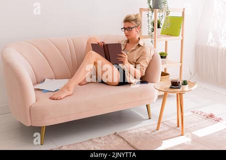 Une femme, assis sur un canapé confortable dans un intérieur lumineux, écrire dans le journal Banque D'Images