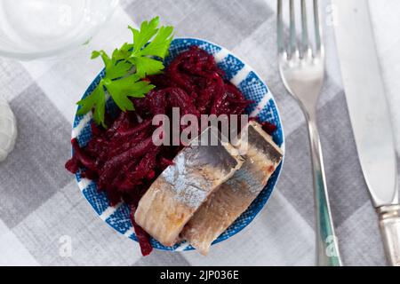 Salade de hareng appétissante avec betteraves, crème sure et persil dans une assiette blanche Banque D'Images