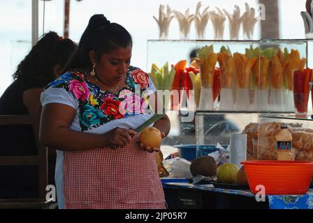 Gros plan d'un vendeur de fruits frais exotiques mexicains pendant qu'elle coupe un pamplemousse : en arrière-plan, des paquets bordeaux de fruits mélangés Banque D'Images