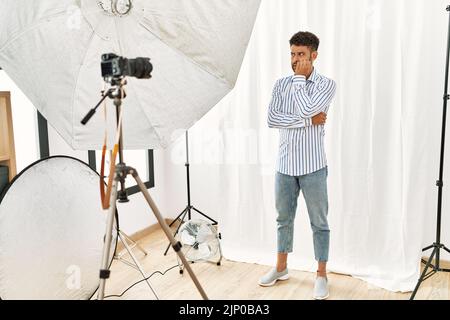 Un jeune arabe qui se pose comme modèle dans un studio de photographie en regardant stressé et nerveux avec les mains sur la bouche piquant les ongles. Banque D'Images