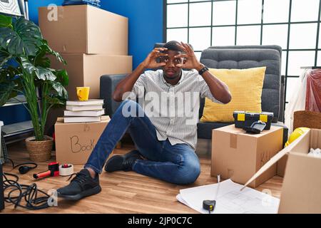 Afro-américain homme assis sur le sol à la nouvelle maison essayant d'ouvrir les yeux avec les doigts, endormi et fatigué pour la fatigue du matin Banque D'Images