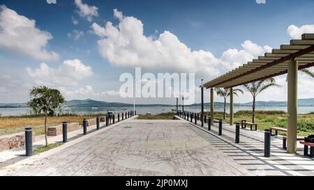 un lagon, avec des bateaux en arrière-plan, un cheval blanc mangeant, une pergola et des bancs sur la droite. une pergola et des bancs Banque D'Images