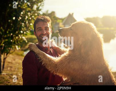 HES un sac de rires. Portrait court d'un beau jeune homme et de son chien passant la journée au bord d'un lac dans le parc. Banque D'Images