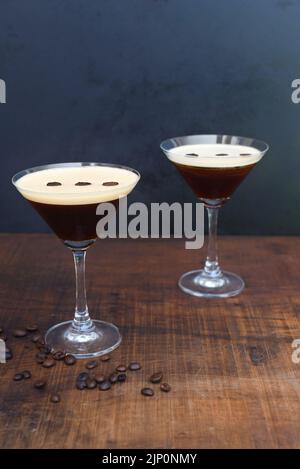 Verres de martini expresso avec grains de café sur table en bois et fond noir Banque D'Images