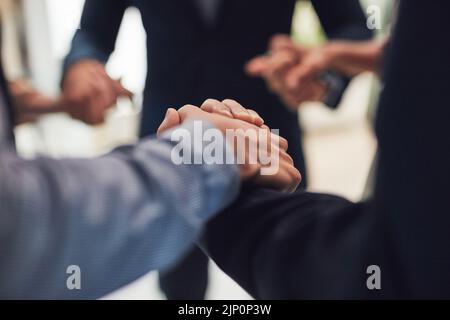 Nous allons nous réunir et travailler. Gros plan d'un groupe d'hommes d'affaires méconnus qui tiennent la main tout en se tenant en cercle dans le bureau pendant le Banque D'Images