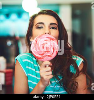 Je suis une petite fille bonbon. Portrait court d'une jeune femme attrayante mangeant un hollipop géant dans un restaurant rétro. Banque D'Images