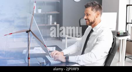 Double exposition de l'homme d'affaires utilisant l'ordinateur dans le bureau et le moulin à vent pour la production d'énergie électrique dans la campagne Banque D'Images