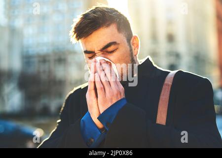 J'espère que ce froid ne m'arrêtera pas de travailler. Un jeune homme irrité qui a l'air de souffler son nez avec un tissu tout en marchant dans les rues animées de la ville Banque D'Images