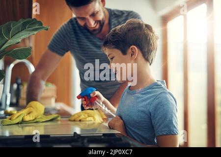 Un père et un fils qui nettoient le comptoir de la cuisine ensemble à la maison s'associent pour s'emparer de ces microbes. Banque D'Images