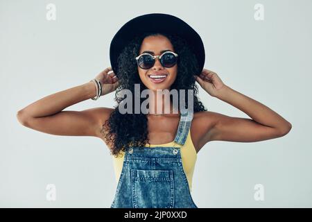 S'amuser avec mon chapeau funky. Photo en studio d'une jeune femme attrayante posant sur un fond gris. Banque D'Images