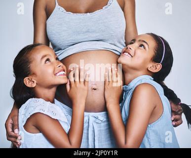 Une famille heureuse. Deux petites filles gaies debout à côté de leur mère enceinte à la maison pendant la journée. Banque D'Images