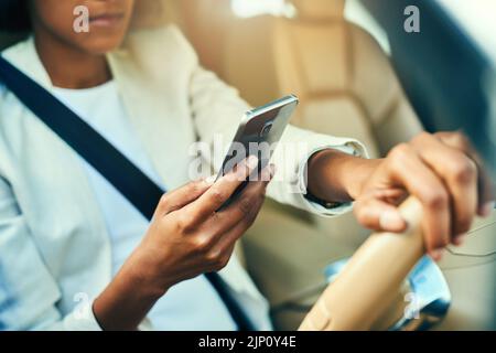 Il semble que la messagerie instantanée soit une surprise au bureau. Une femme d'affaires méconnaissable navigue sur son téléphone mobile tout en conduisant dans une voiture pendant la journée. Banque D'Images