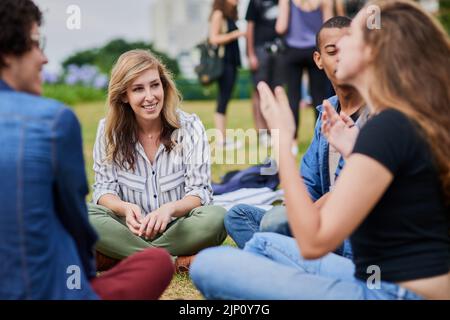 Un groupe de jeunes étudiants qui étudient ensemble tout en étant assis dans un parc à l'extérieur pendant la journée. Banque D'Images