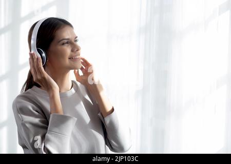 Bonne jeune femme portant des écouteurs écouter de la musique tout en dansant et chantant avec plaisir et de profiter dans le salon, la femme de bonheur avec le divertissement Banque D'Images