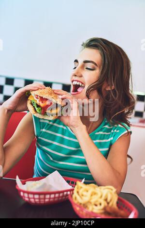 Maintenant c'est une petite femme qui apprécie un hamburger dans un restaurant rétro. Banque D'Images