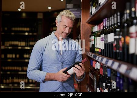 Cela va bien pair avec le steak que j'ai acheté. Un beau homme mature achetant du vin à une épicerie. Banque D'Images