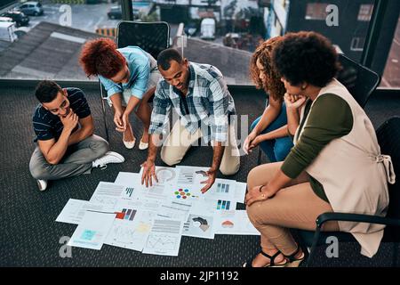 Expliquer en détail. Un groupe de jeunes collègues focalisés travaillant ensemble et brainstorming tout en étant assis sur le plancher du bureau au travail Banque D'Images