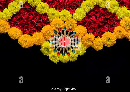 Fleurs de marigold et roses décoratives rangoli pour le festival de Diwali avec lampe diya éclairée avec une flamme floue sur fond noir. Banque D'Images