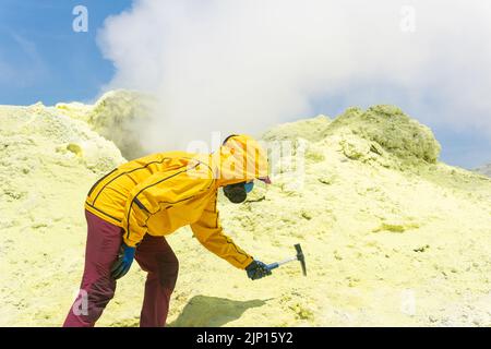 une femme volcanologue sur la pente d'un volcan à côté d'un fumarale fumarate prend un échantillon d'un minéral au bord d'un cratère sulfureux Banque D'Images