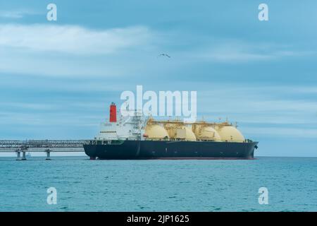 Camion-citerne de transport de gaz naturel liquéfié pendant le chargement à un terminal offshore de GNL, à la distance où le terminal d'exportation de pétrole est visible dans la mer Banque D'Images