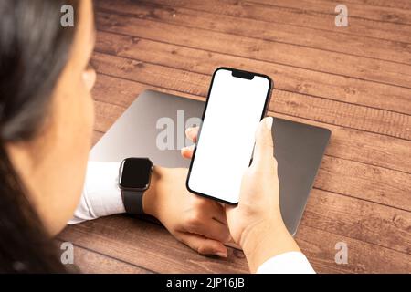 Femme tenant un smartphone, vue sur l'épaule d'une femme tenant un smartphone. Femme caucasienne portant une montre intelligente et un écran blanc. Banque D'Images