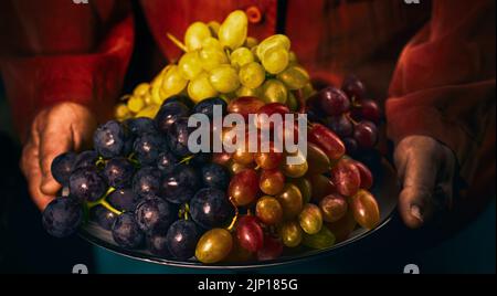Une femme anonyme tient une assiette avec des grappes de raisin noir, blanc et rose dans ses mains Banque D'Images