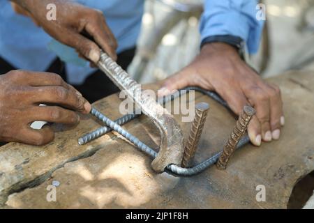 L'ouvrier plie la tige en acier à l'aide d'un outil de pliage sur un chantier de construction. Gros plan de la main mâle avec barre d'armature en métal cintrage avec main-d'œuvre manuelle. Le ouvrier Banque D'Images