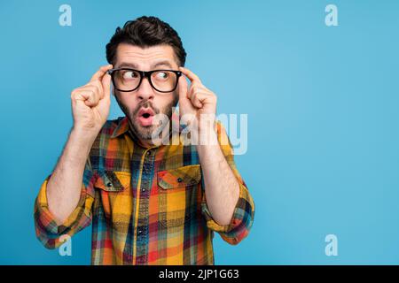 Photo d'un homme élégant et impressionné chemise habillée à carreaux look vide espace tactile lunettes isolées sur fond bleu Banque D'Images