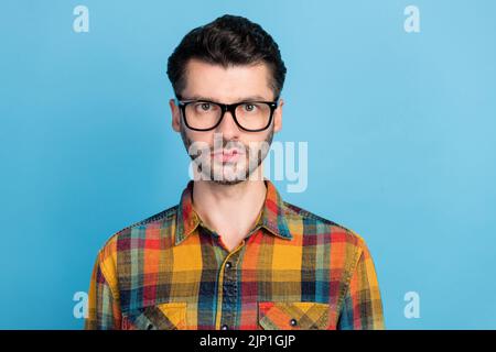 Photo d'un jeune homme beau barbu en lunettes vêtu d'une chemise à carreaux debout regarder un appareil photo isolé sur fond bleu Banque D'Images