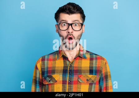 Photo de l'élégant beau homme étonné habillé lunettes costume damier chemise impressionné regardant la caméra isolée sur fond bleu de couleur Banque D'Images