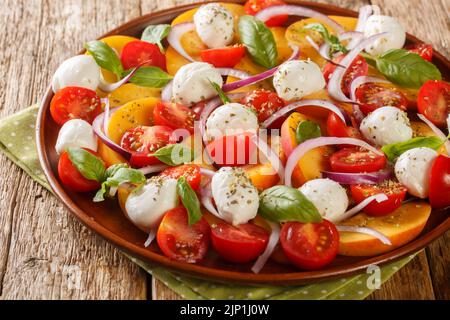 Salade de pêche d'été Caprese avec mozzarella et tomates cerises dans une assiette sur une table en bois. Horizontale Banque D'Images