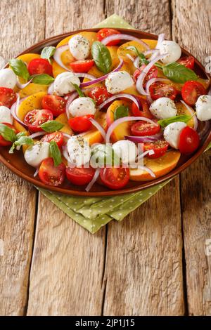 Salade d'été avec pêches fraîches, mozzarella, tomates cerises, oignon et basilic dans une assiette sur une table en bois. Verticale Banque D'Images