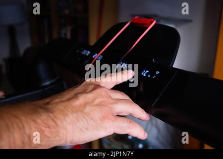 Vue rognée du sportif en appuyant sur le bouton du capteur sur le panneau de commande du tapis roulant Banque D'Images