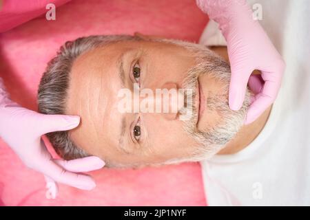 Les mains d'une esthéticienne vérifient la peau du visage de l'homme Banque D'Images