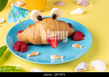 Nourriture amusante pour les enfants - croissant en forme de crabe avec fraise et banane sur fond jaune Banque D'Images
