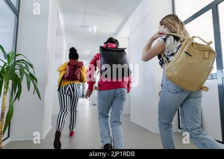 Vue arrière des jeunes élèves du secondaire qui marchent dans le couloir à l'école, concept de retour à l'école. Banque D'Images