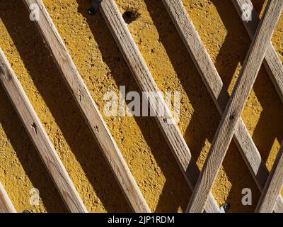 Des planches diagonales en bois sont en grille sur un mur en béton jaune Banque D'Images