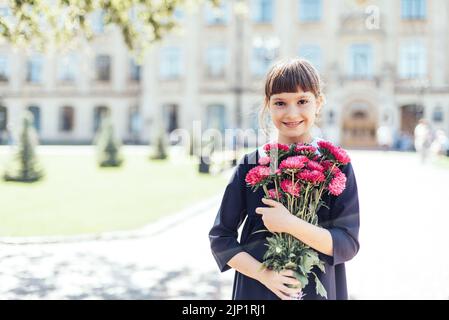 Bouquet pour professeur bien-aimé le premier septembre. Fleurs pour la dernière cloche. Jour de la connaissance. Début de l'année scolaire. Écolière avec bouquet en uniforme scolaire sur fond d'école Banque D'Images