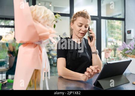 Un fleuriste amical prend la commande en ligne et saisit les données dans la tablette Banque D'Images