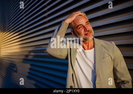 Homme d'affaires mature et détendu, reposant sur le mur de la rue pendant un beau coucher de soleil, concept d'équilibre entre vie professionnelle et vie privée. Banque D'Images