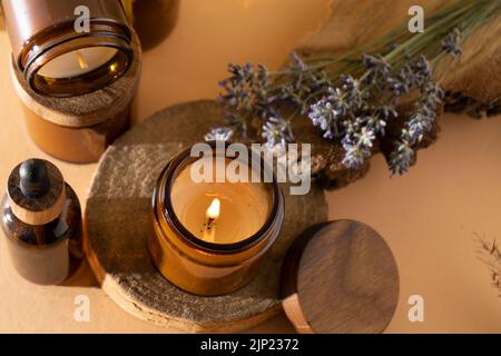 Bougies de soja dans un pot en verre. Aromathérapie. Bougie brûlante et lavande. Couvercle en bois pour bocaux. Arrière-plan beige. Confort et détente. Fait à la main. Décoration d'intérieur. Banque D'Images