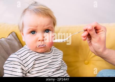 Maman nourrit un petit enfant à la maison avec du yaourt à la cuillère. Concept de famille Banque D'Images