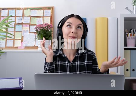 Une jeune femme heureuse, qui porte un casque sans fil, cherche à discuter avec ses clients en ligne et à travailler à distance sur son lieu de travail depuis chez elle Banque D'Images