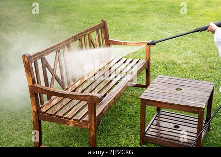 Vue rapprochée de la personne travaillant nettoyage pression lavage meubles de jardin en bois banc extérieur en été. Banque D'Images