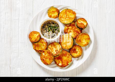 Hobak Jeon, courgettes poêlées dans une pâte à œufs, servies avec une sauce soja sur une assiette en bois blanc, cuisine coréenne, vue horizontale depuis le dessus, Banque D'Images