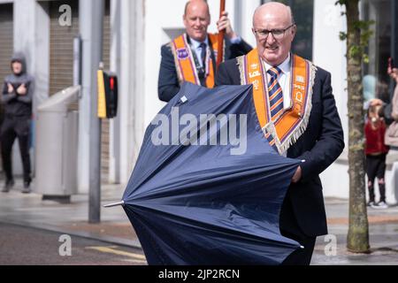 Ballymena, Royaume-Uni, 25th juin 2022. Soleil et averses pendant que Orangeman ferme son parapluie à Broadway - pendant la mini-douzième parade annuelle. Banque D'Images