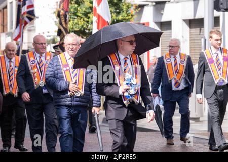 Ballymena, Royaume-Uni, 25th juin 2022. Maître Worshipful de Ballygarvey Lodge prend refuge sous parapluie pendant une brève douche de pluie à la mini-douzième année. Banque D'Images