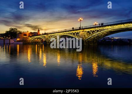 Pont de Triana à Séville au-dessus du fleuve Guadalquivir au coucher du soleil, avec des lumières reflétant dans l'eau du fleuve, une scène idyllique et charmante. Andalousie. Banque D'Images